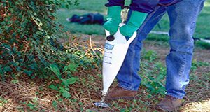 A photo of a person in protective gloves using a manually-pumped applicator to inject pesticides into the soil.