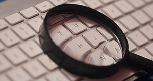 A close up of a magnifying glass lying on a computer keyboard.