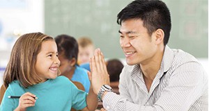 a photo of an elementary student sharing a "high five" with an adult in a classroom setting