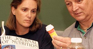 two people looking at the instructions on a bottle of medicine, while one refers to The Journal of Nutrition