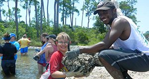 A photo of a group of people working together in water and on shore to place oysters in mesh bags for living shoreline.