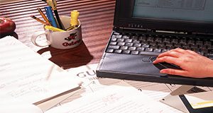 photo of a hand using a laptop on a cluttered desk