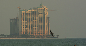 A photo of a multistory beachfront hotel or condominium at sunset with construction cranes, ocean in the foreground.