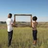 A man and woman holding a picture frame in a feild.