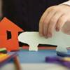 A child playing with paper cutouts of a house and car.