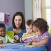 A woman sitting at a table with toddlers who are coloring.