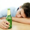 A teenage boy with a beer in his hand and his head down on a table.