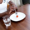 A girl eating a meal of a cherry tomato and glass of water.