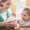 A woman showing her young daughter a piggy bank.