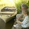 A boy and his grandfather fishing from the side of a lake.