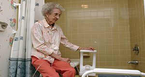 An elderly women sitting on the edge of a bathtub 