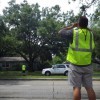 A man in a safety vest looking at a tree in front of the house across the street.