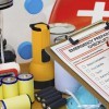 Someone holding a clipboard with an emergency preparation checklist by a bunch of emergency supplies