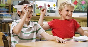 Two young boys in a classroom about to throw paper airplanes
