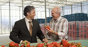 A man showing off a red bell pepper to another man