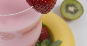 Strawberries, kiwi fruit, wheat grass, a banana, and a strawberry flavored milk shake.