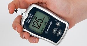 Hand held electronic diabetes monitoring device pricking a finger. The number on the screen reads 125.