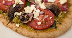 Tomato, mushroom, pesto, and feta cheese on a whole grain flatbread.