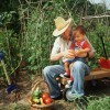 Anciano con un niño sentado en su regazo y productos agrícolas en una canasta a sus pies.