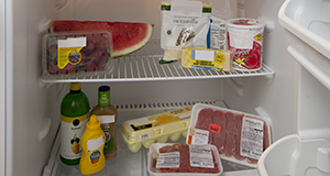 Two shelves of a refrigerator containing fruits and dairy items on the top shelf and condiments, dressings, eggs, and meats on the bottom shelf.